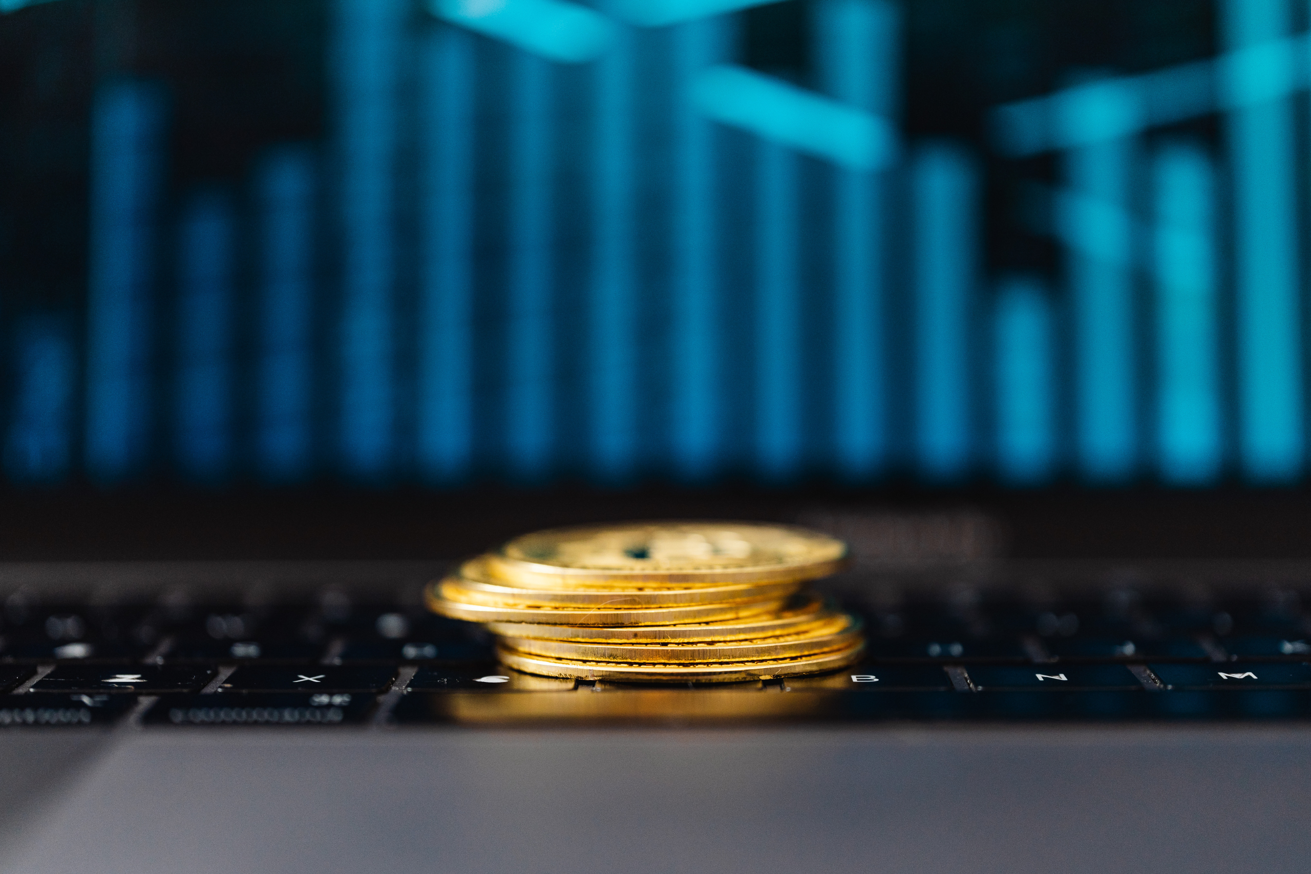 Stos złotych monet leżących na klawiaturze laptopa, na tle wykresu finansowego symbolizującego analizę danych i controlling.